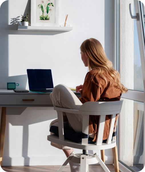 Woman in a gray swivel chair, looking at a laptop at a table.