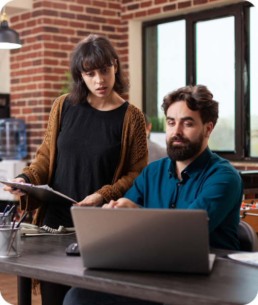 Man and woman reviewing information on a laptop, woman holding a clipboard.