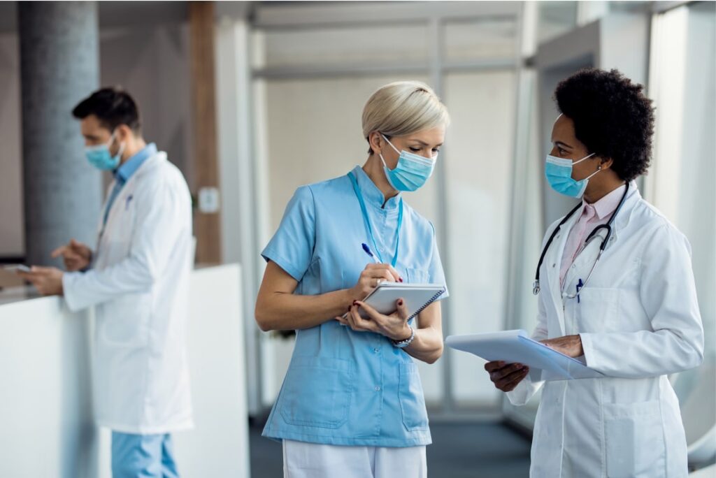 Two female healthcare workers consulting a chart together while a male healthcare worker reviews documents at a station.