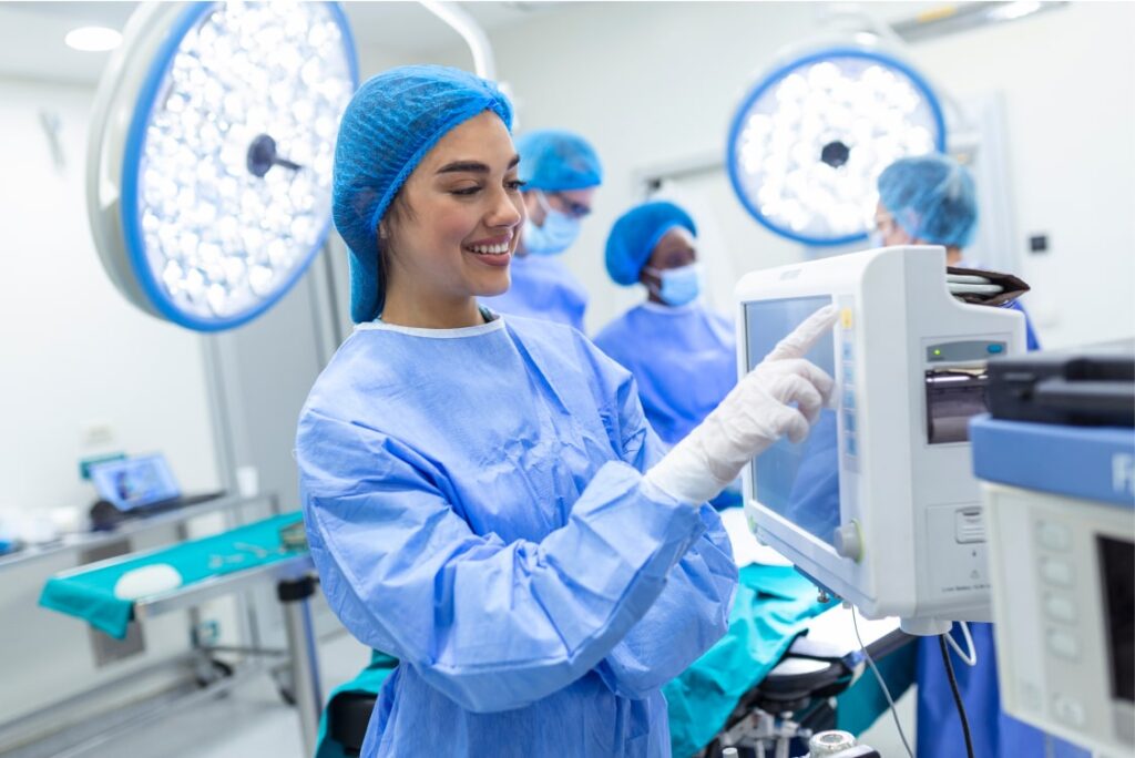 Smiling female healthcare worker operating a touch screen on medical monitoring equipment in an operating room