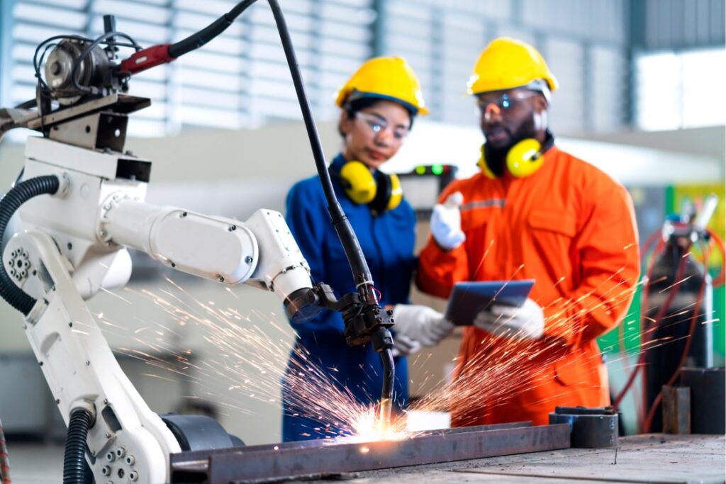 Male and female manufacturing workers observing a robot welding on a production line.